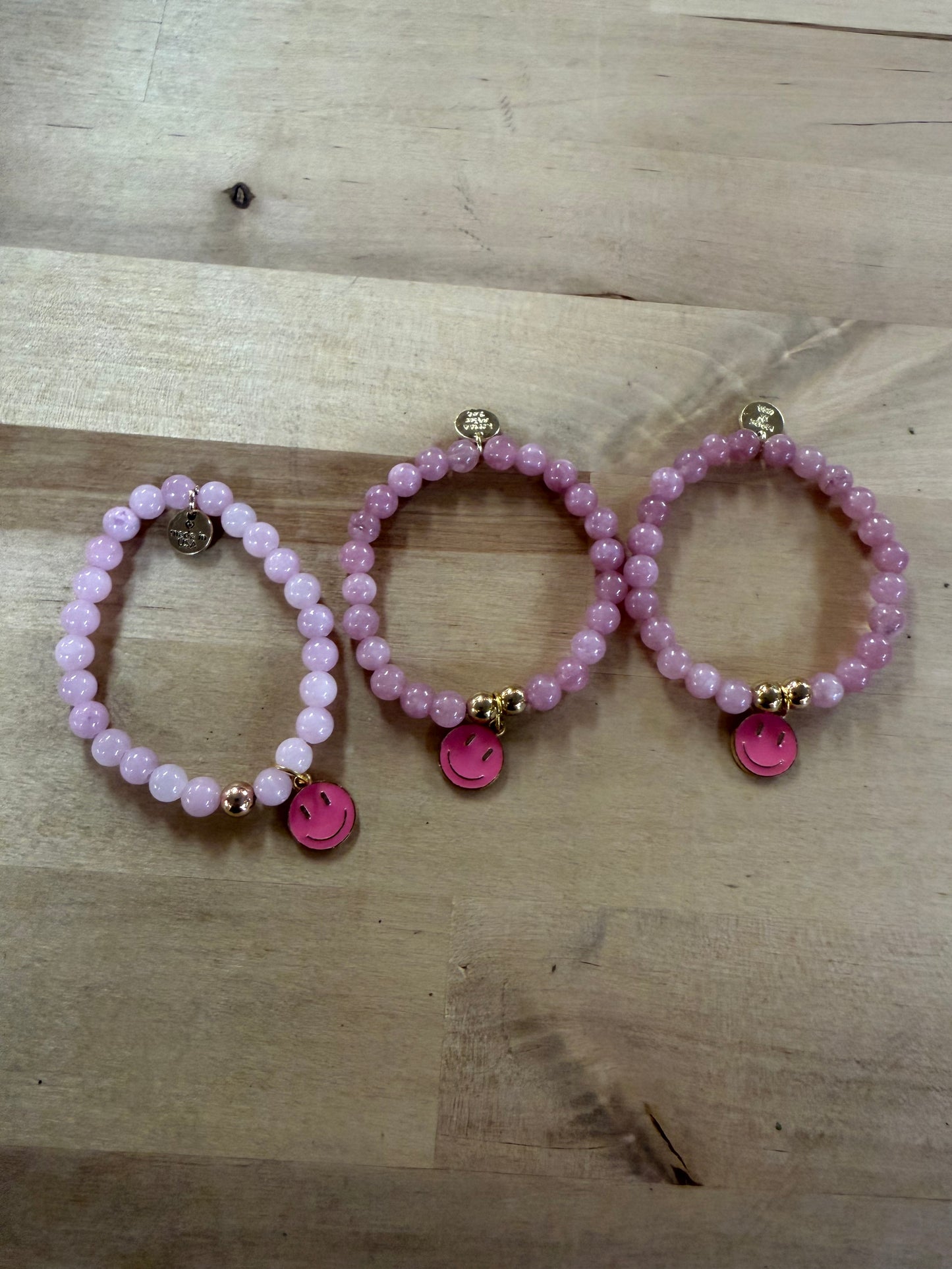 Three pink beaded stretch bracelets with hot pink smiley face charms and gold accents