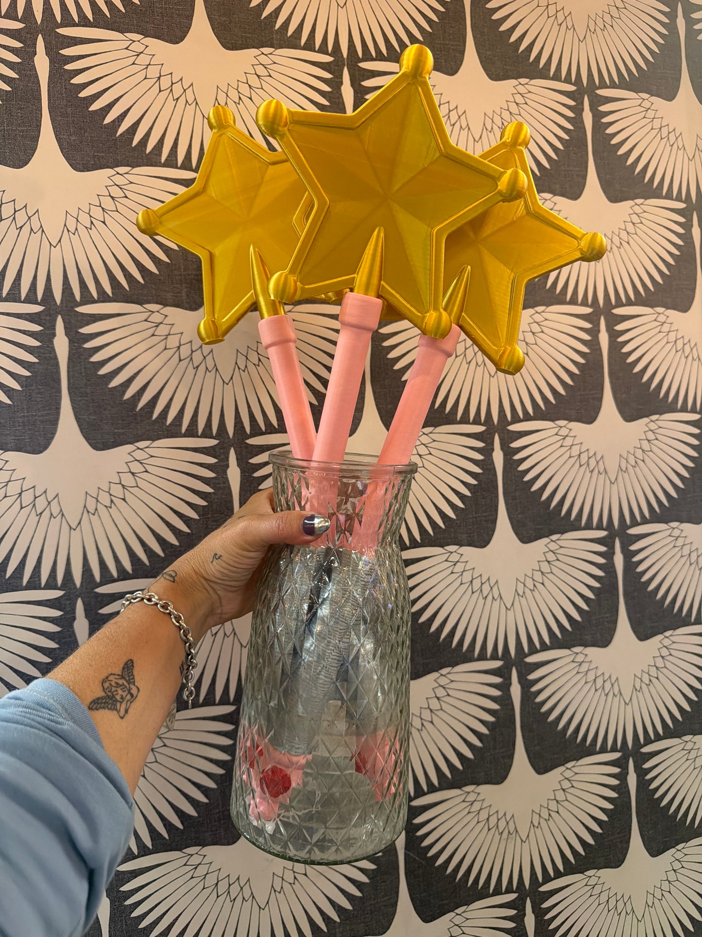 Three gold star-topped pink magic wands displayed in a glass jar