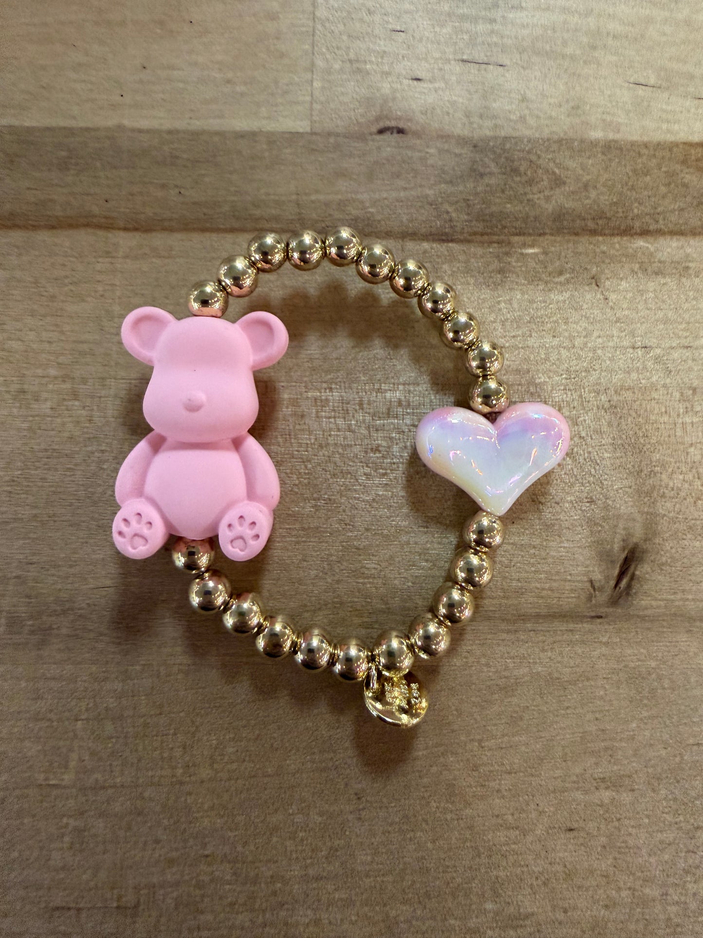 Gold beaded stretch bracelet with pink teddy bear charm and iridescent heart charm