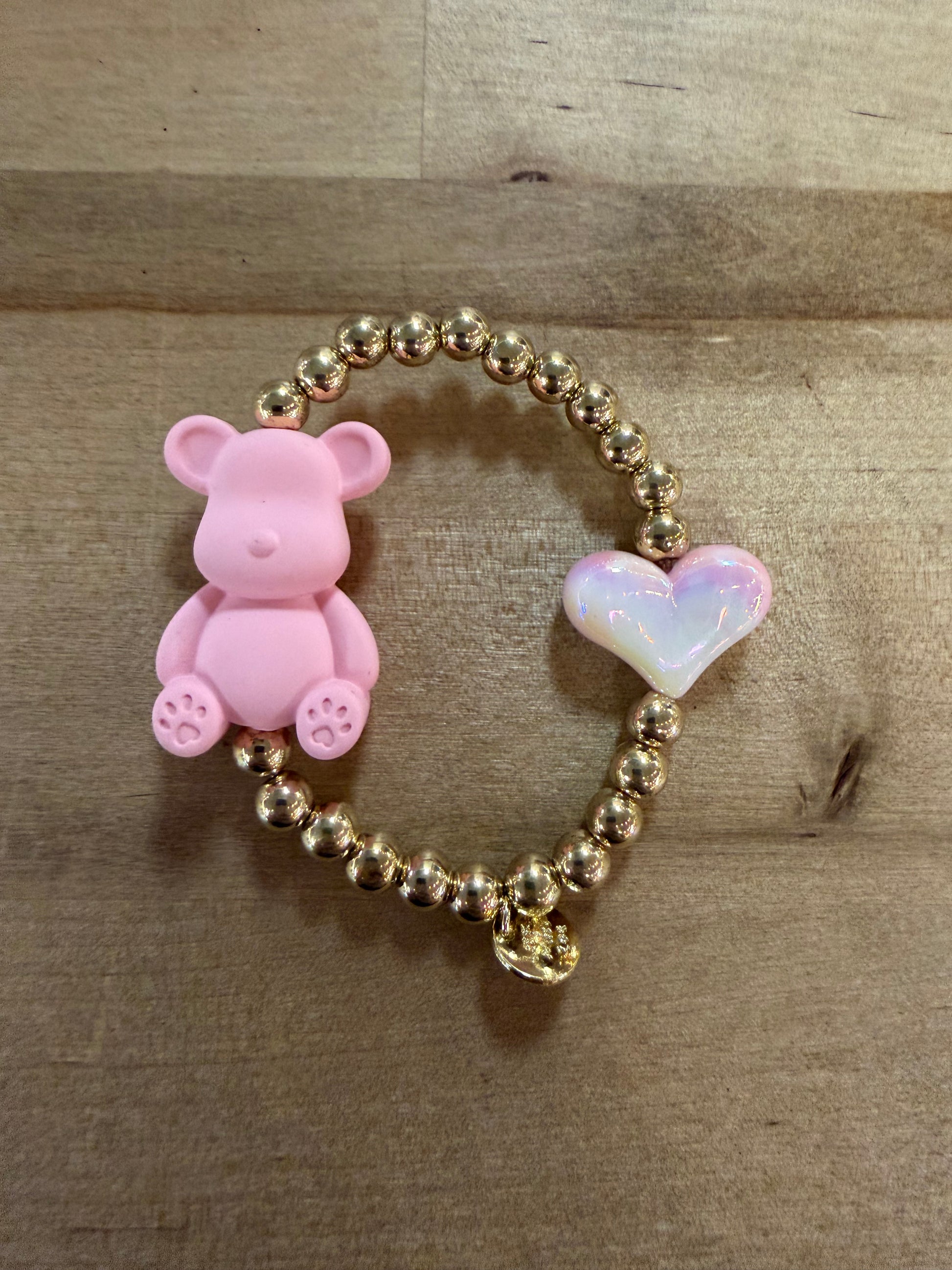 Gold beaded stretch bracelet with pink teddy bear charm and iridescent heart charm