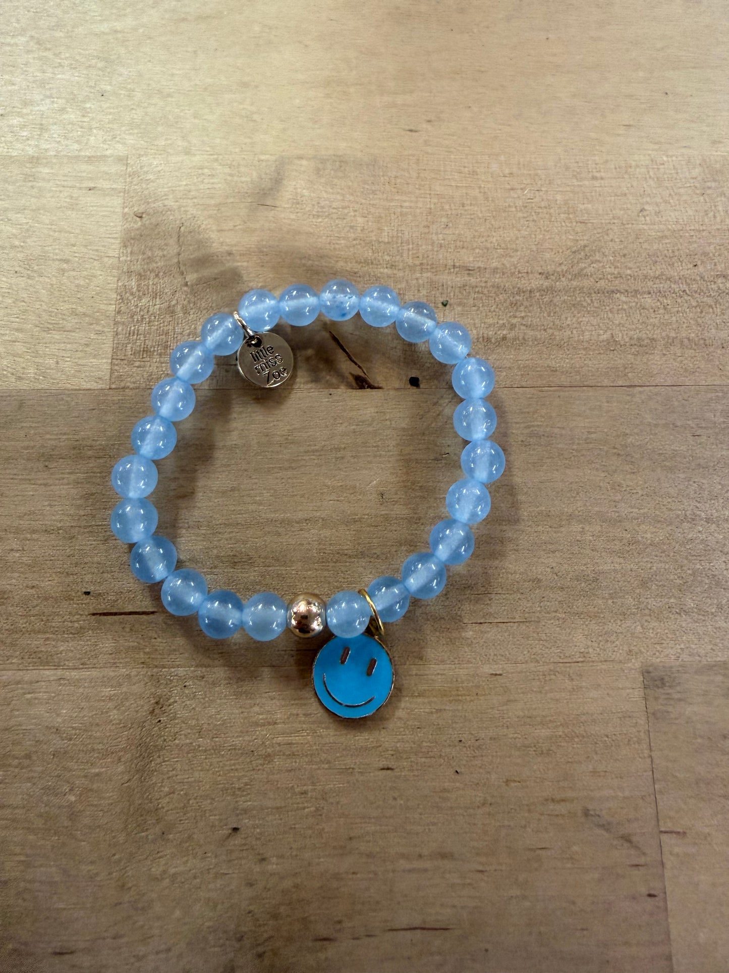 Light blue beaded stretch bracelet with a turquoise enamel smiley face charm