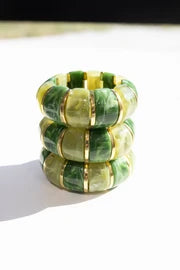 Three stacked green and yellow marbled resin stretch bracelets with gold accents
