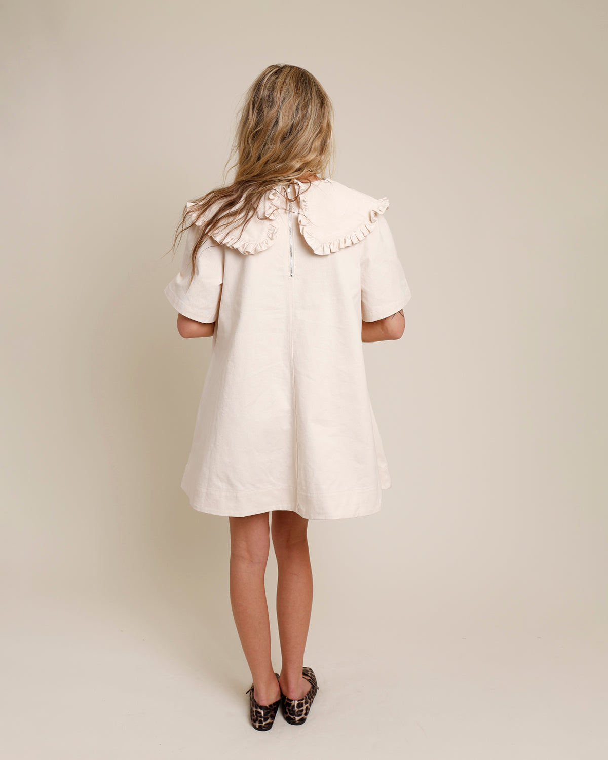 Cream mini dress with ruffle collar, short sleeves, A-line silhouette, back view