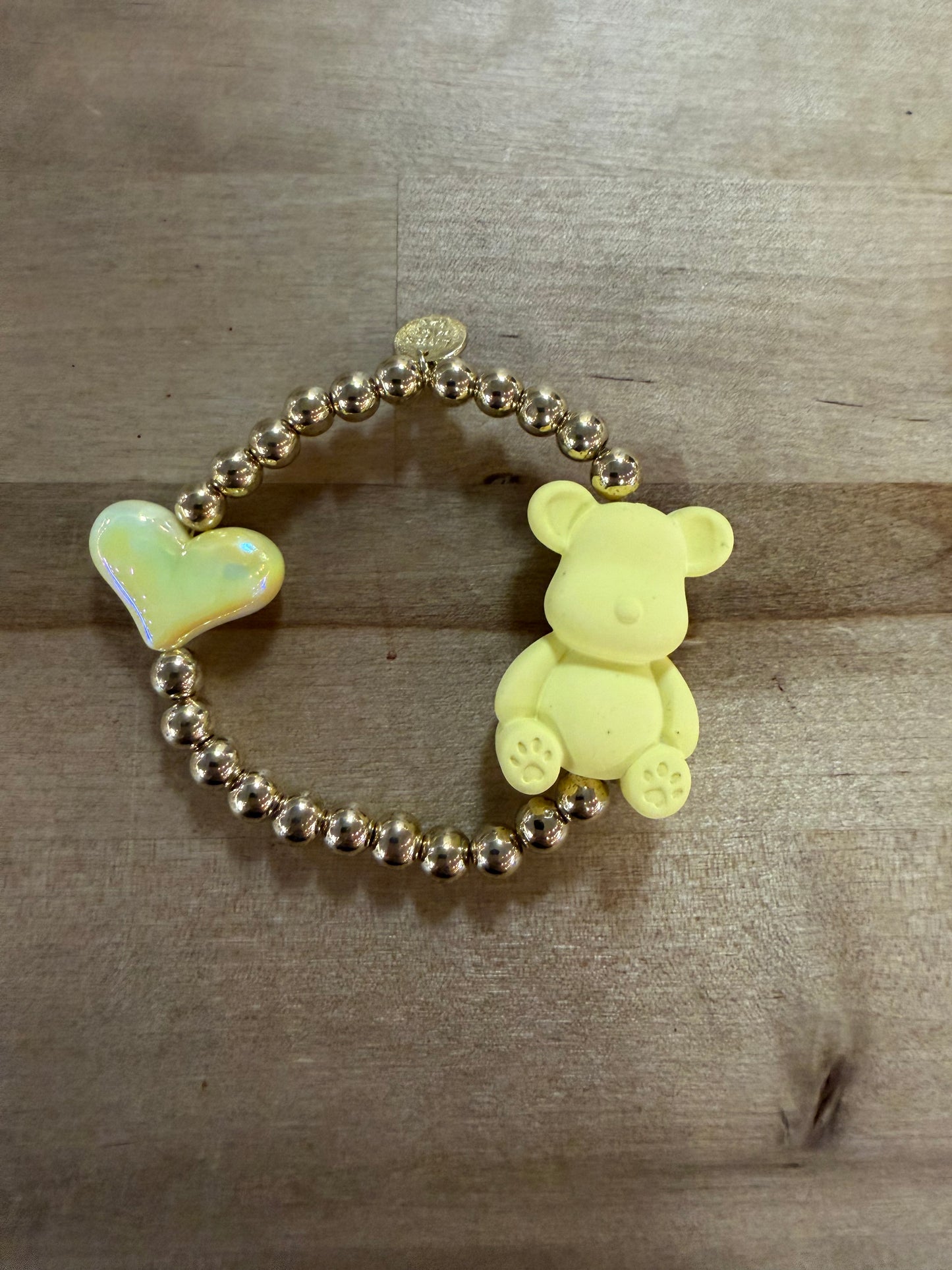 Gold beaded stretch bracelet with yellow bear charm and iridescent heart charm