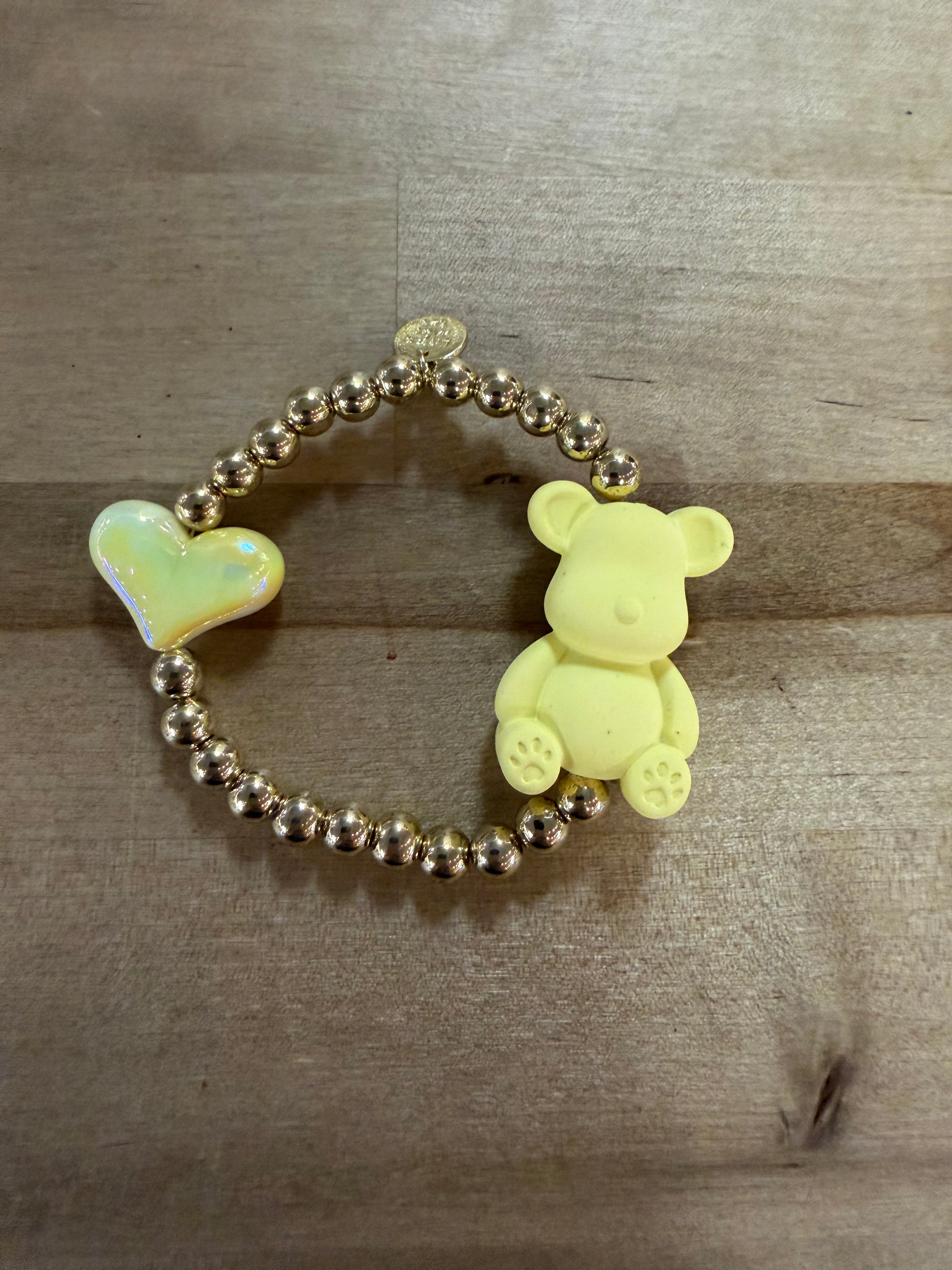 Gold beaded stretch bracelet with yellow bear charm and iridescent heart charm