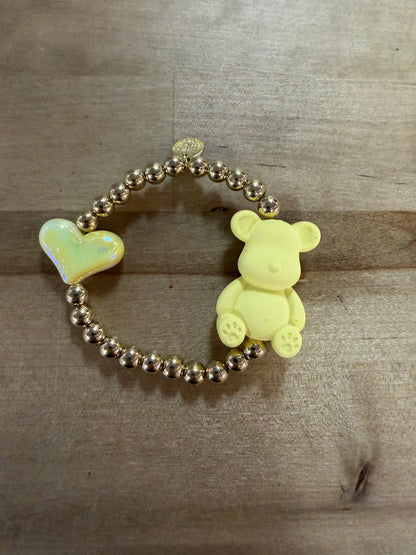 Gold beaded stretch bracelet with yellow bear charm and iridescent heart charm