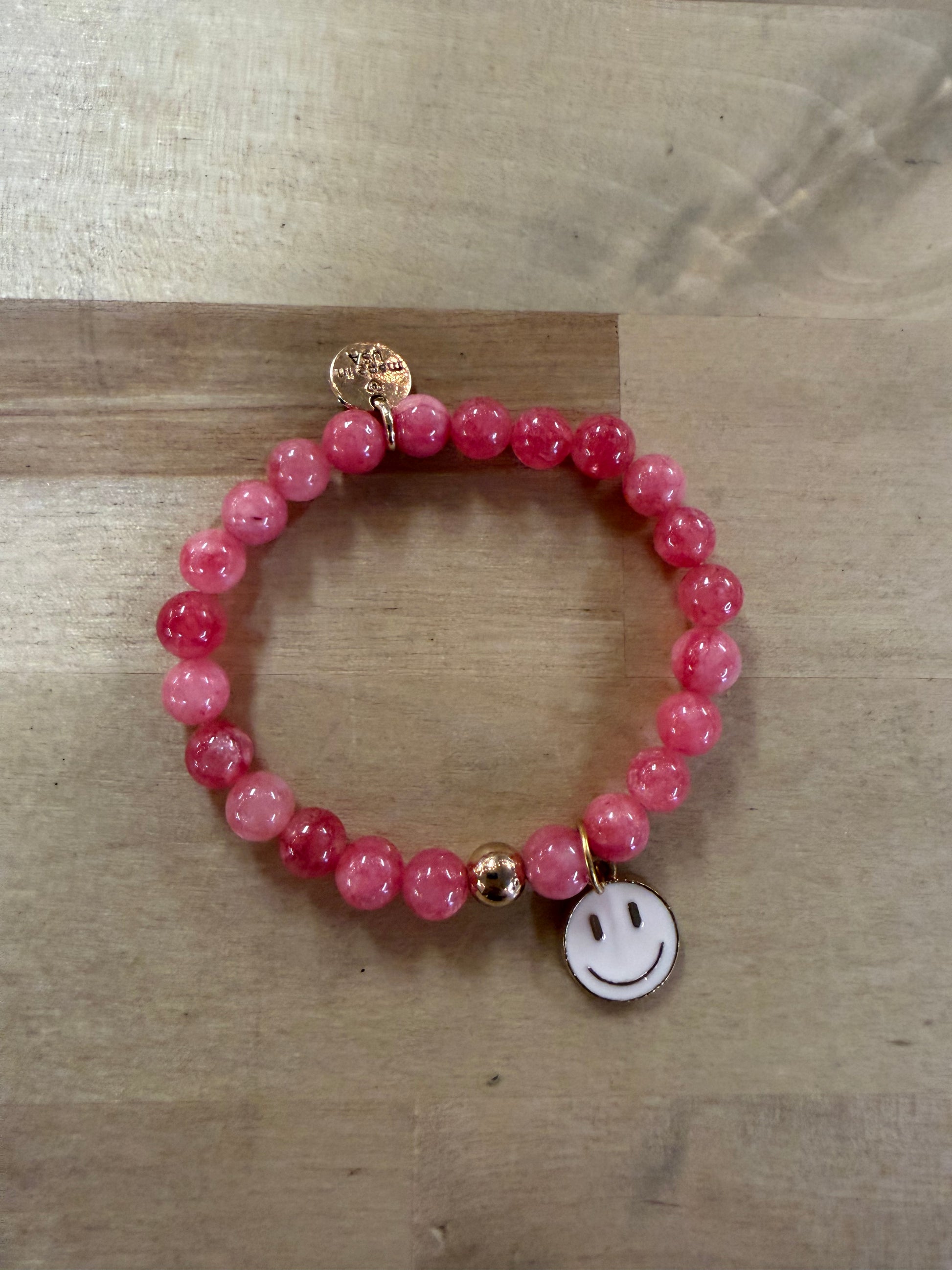Pink beaded stretch bracelet with gold accents and white smiley face charm