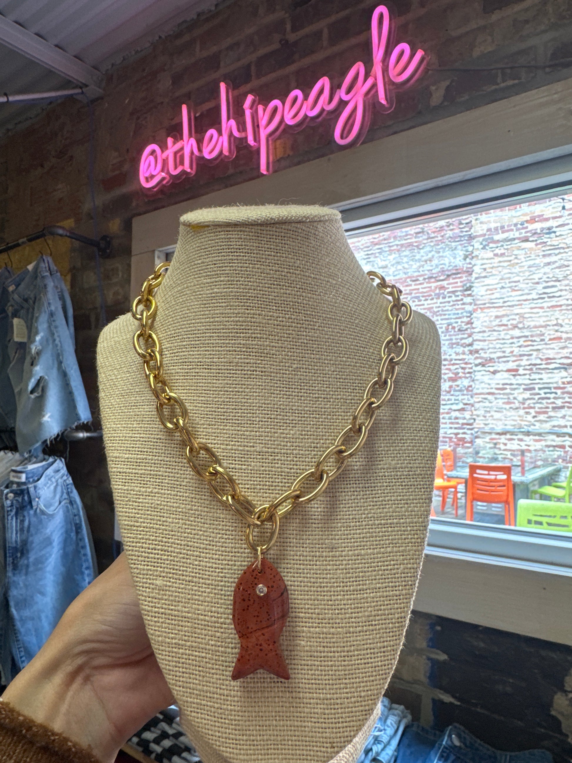Gold chunky chain necklace with red speckled fish pendant on linen bust