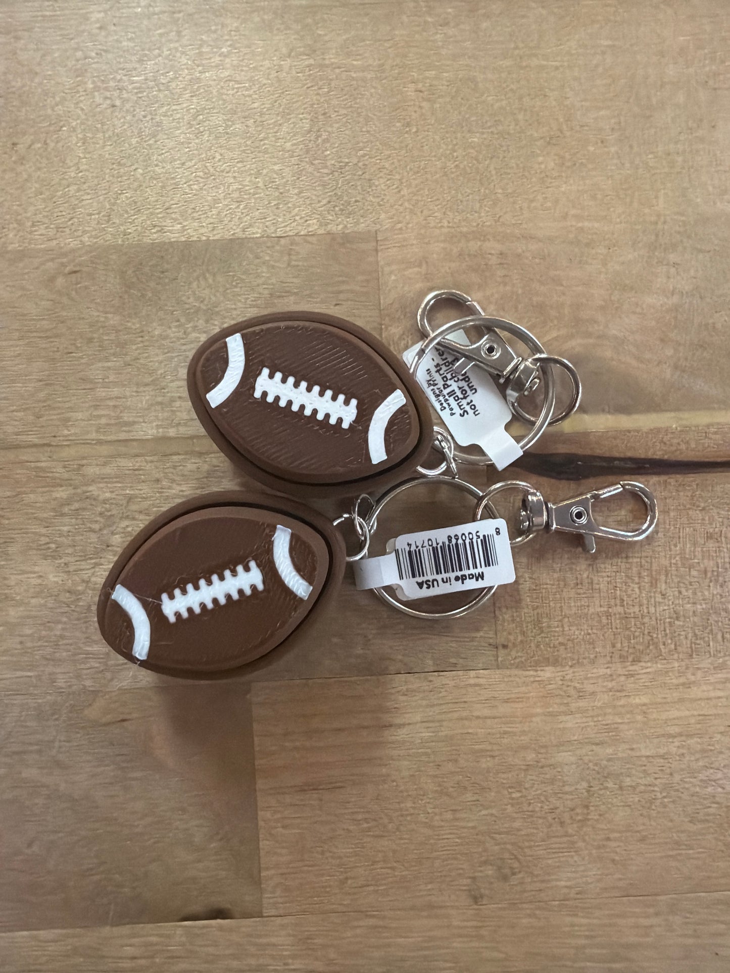 Two brown rubber football keychains with white laces and silver swivel clips