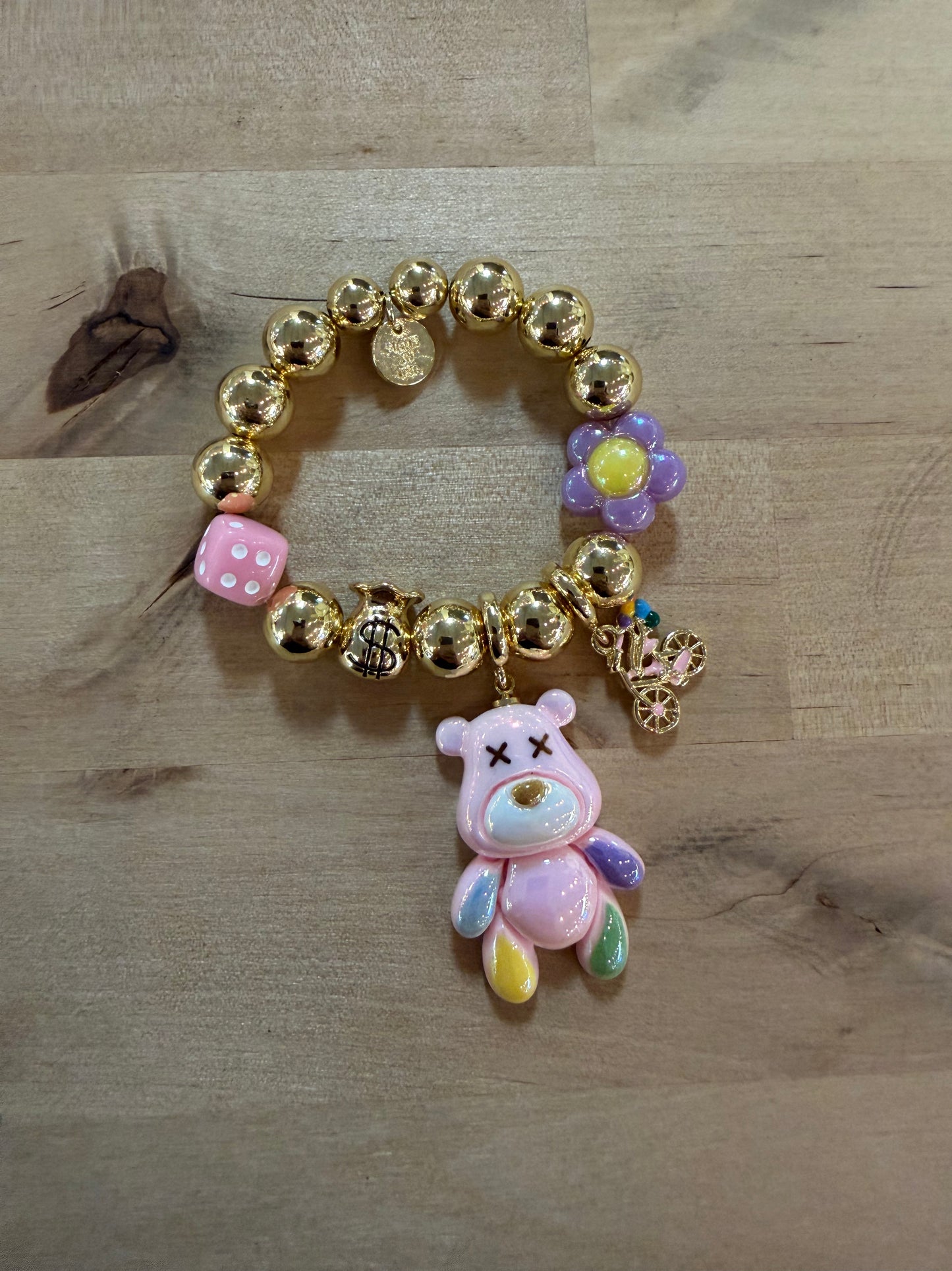Gold beaded charm bracelet with pink bear pendant, dice, dollar bag, and flower charms