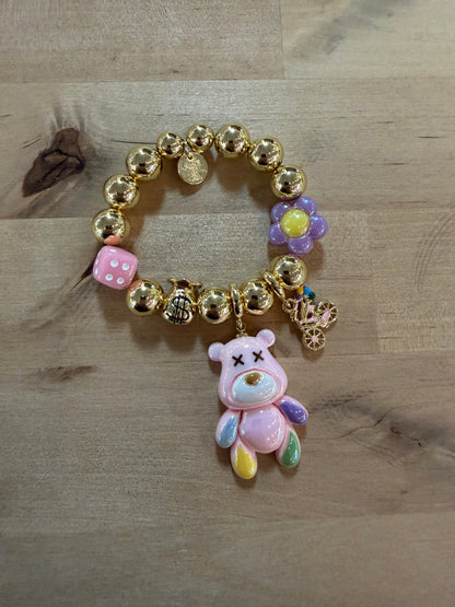 Gold beaded charm bracelet with pink bear pendant, dice, dollar bag, and flower charms