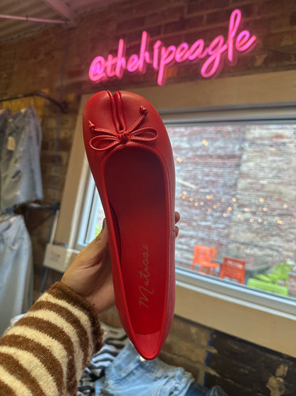 Red split-toe ballet flat with bow detail, held up in boutique setting