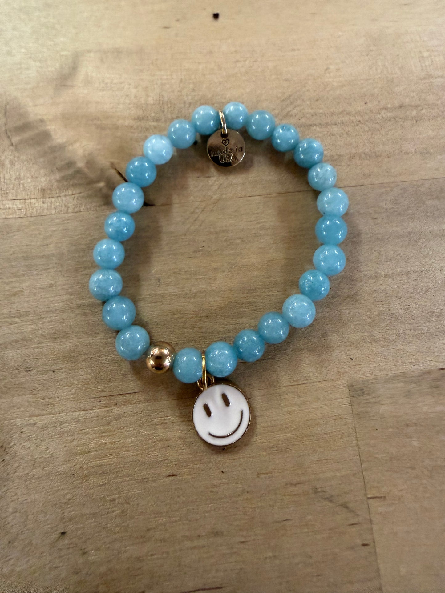 Light blue beaded stretch bracelet with gold bead and white enamel smiley face charm
