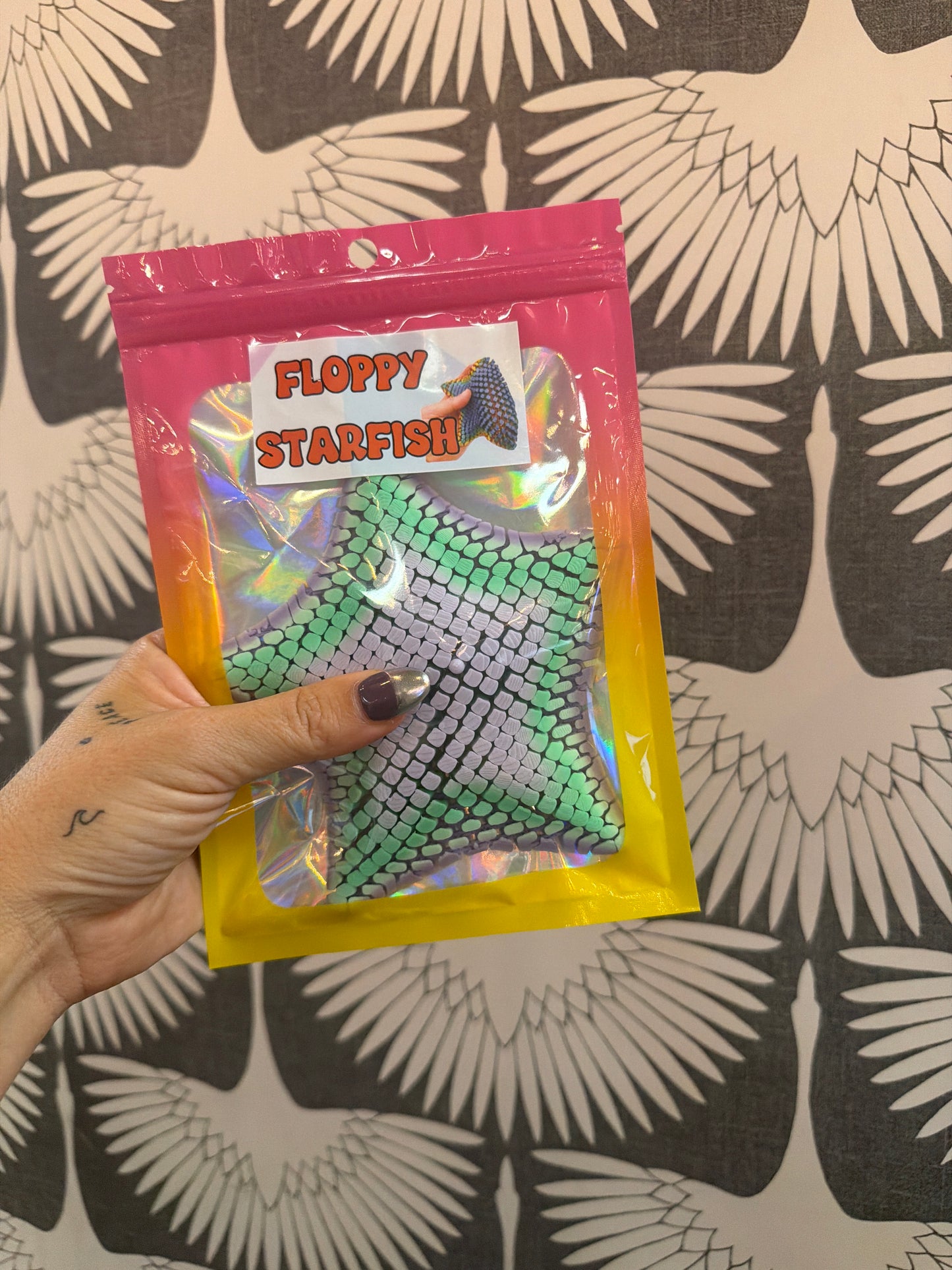 Floppy Starfish fidget toy in green scale-textured flexible silicone, packaged in holographic bag