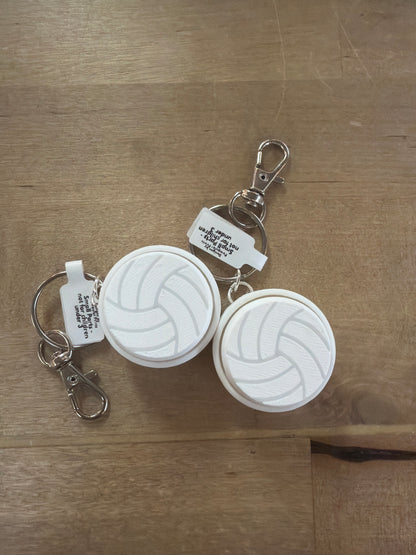Two white volleyball-shaped clicker keychains with silver lobster clasp rings on wood surface