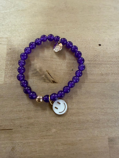 Purple beaded stretch bracelet with gold accent bead and white enamel smiley face charm