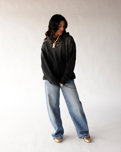 Oversized black washed hoodie styled with wide-leg light blue jeans and gold flats.