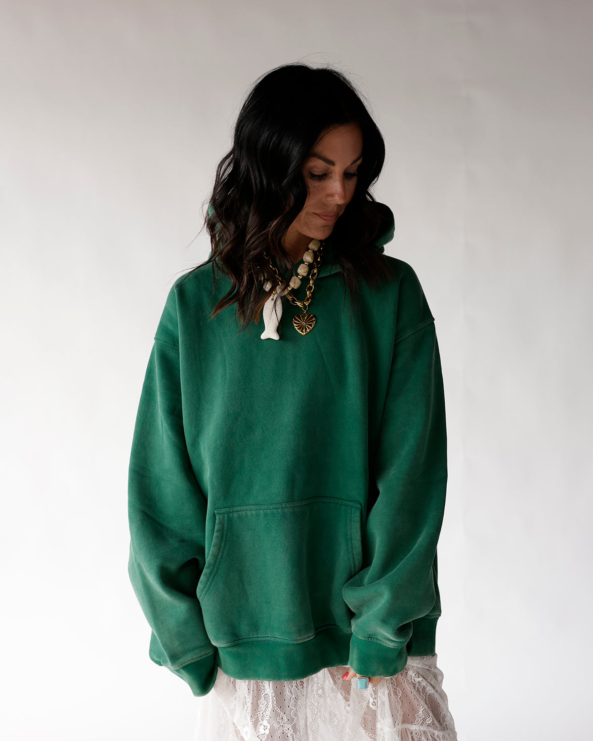 Oversized green hoodie with front pocket, worn with lace skirt and layered necklaces