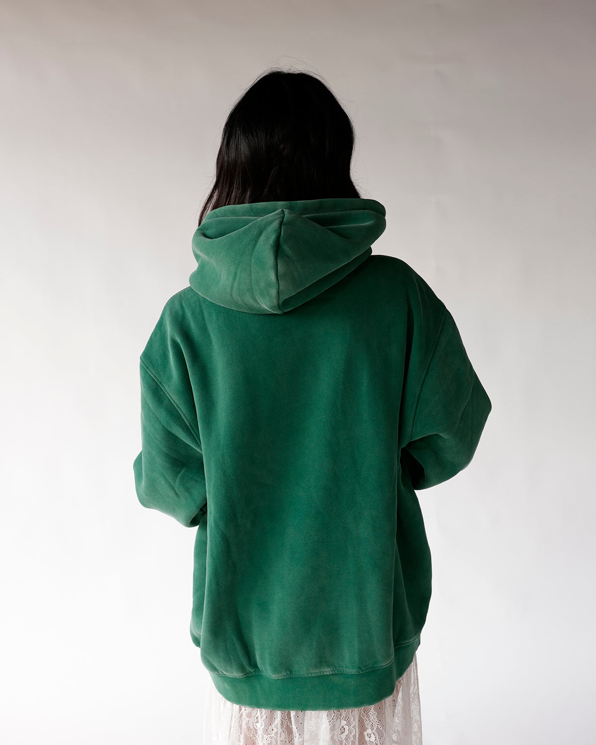 Back view of oversized green fleece hoodie with hood up, worn over lace skirt
