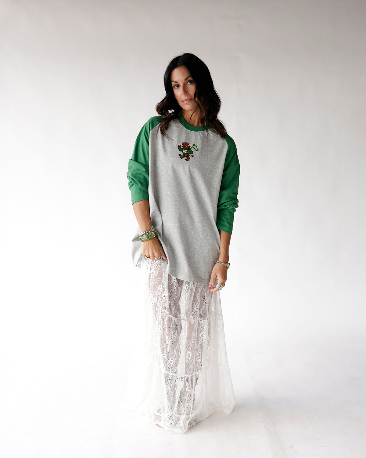 Gray and green raglan long sleeve tee with small mascot graphic, worn over white lace maxi skirt