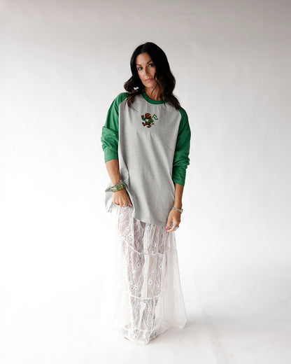Gray and green raglan long sleeve tee with small mascot graphic, worn over white lace maxi skirt