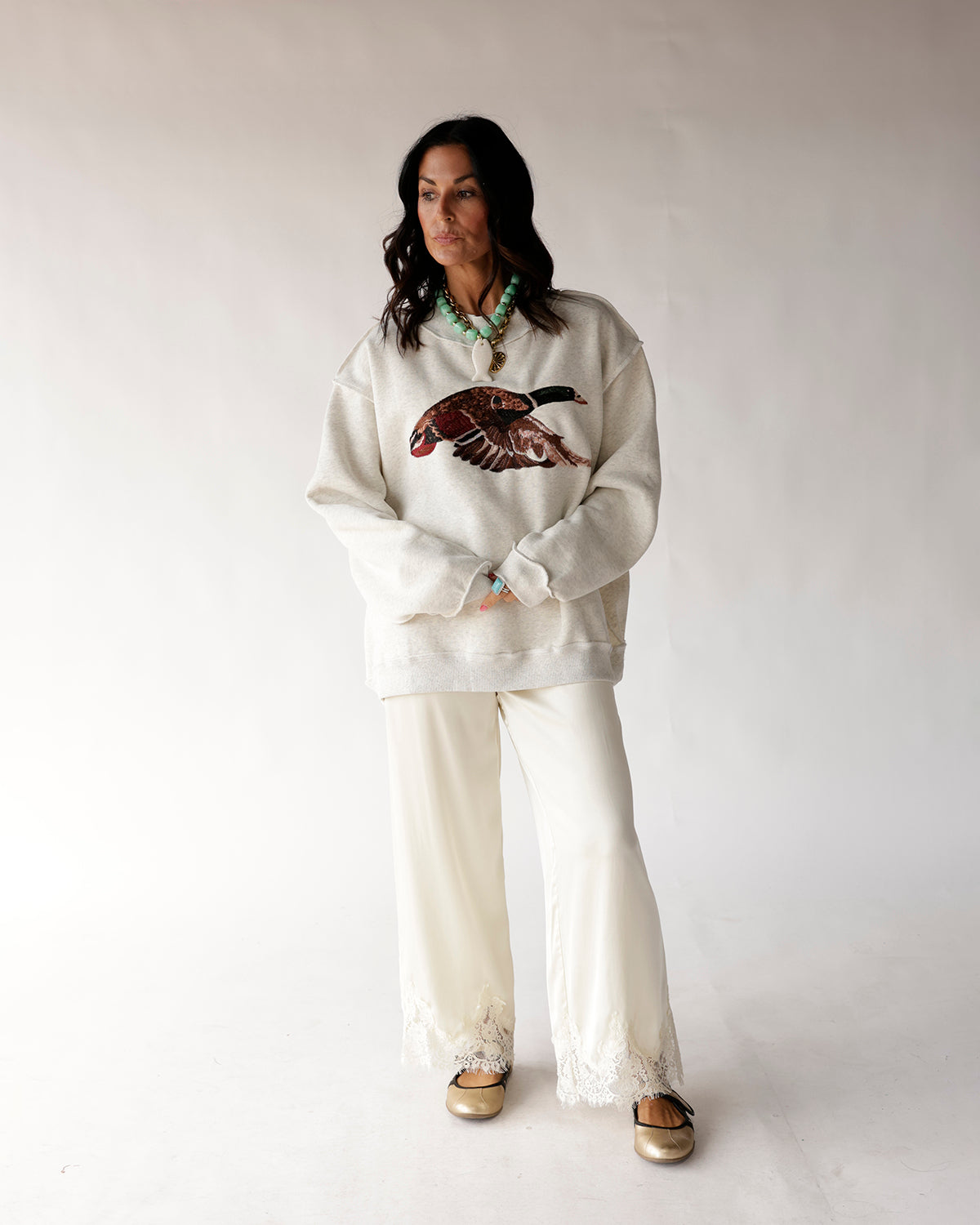 Oatmeal mock neck sweatshirt with mallard duck graphic, worn with cream wide-leg pants