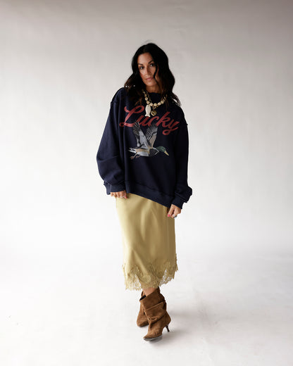 Oversized navy sweatshirt with duck graphic and Lucky script, worn with slip skirt