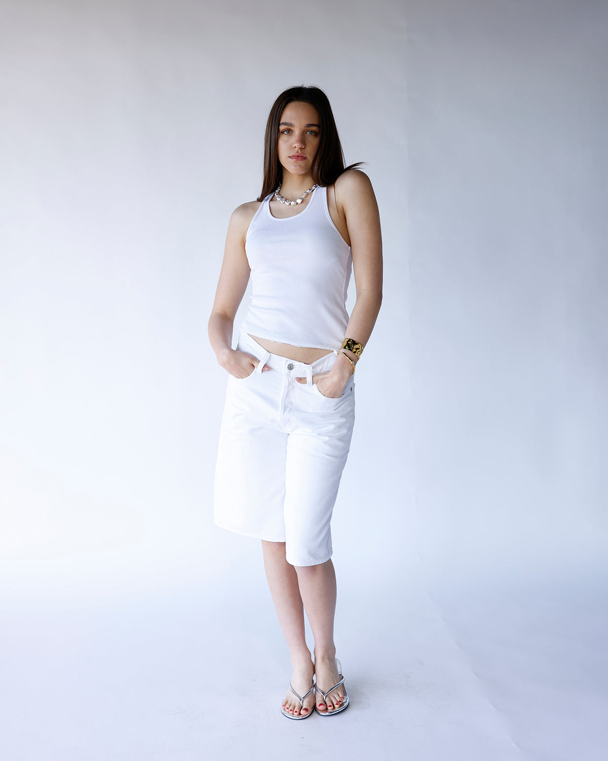 White knee-length denim shorts with five-pocket styling and silver button closure.