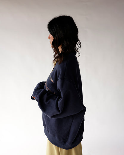 Oversized navy blue mock neck sweatshirt with graphic print, worn as side profile