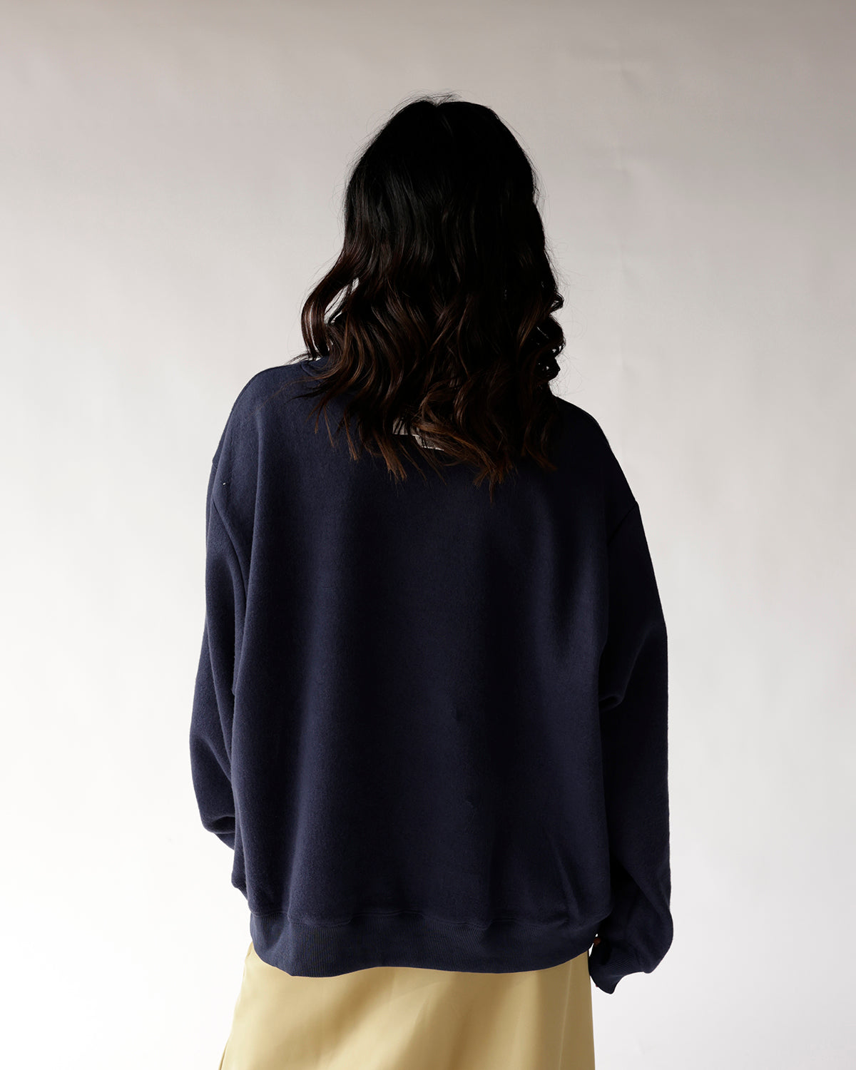 Back view of navy blue oversized crewneck sweatshirt paired with tan skirt