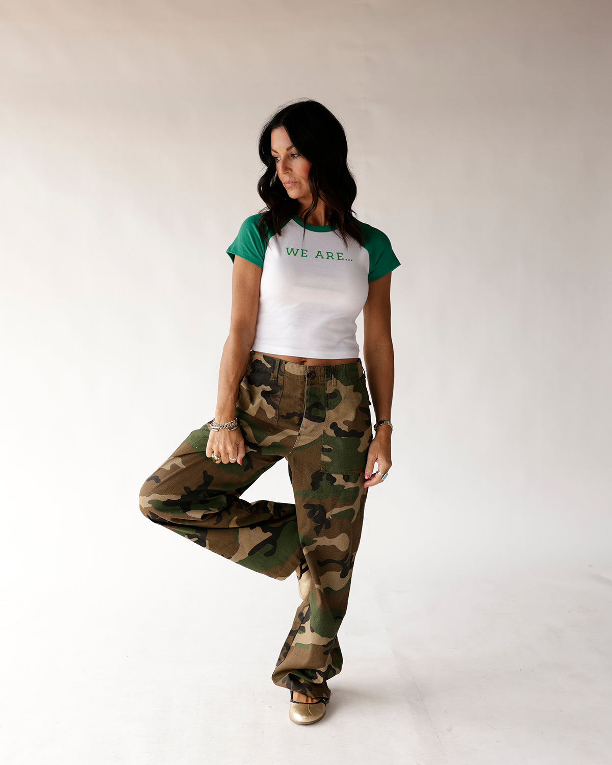 White and green raglan baby tee with 'WE ARE...' text, paired with camo pants