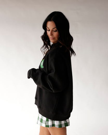 Black mock neck sweatshirt with green patch, paired with green plaid mini skirt