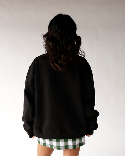 Oversized black mock neck sweatshirt shown from the back, paired with green plaid skirt.