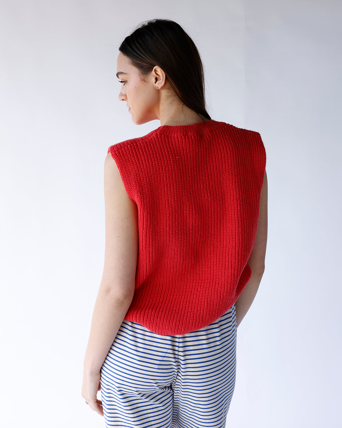 Red ribbed knit sleeveless sweater vest, back view, paired with blue striped pants
