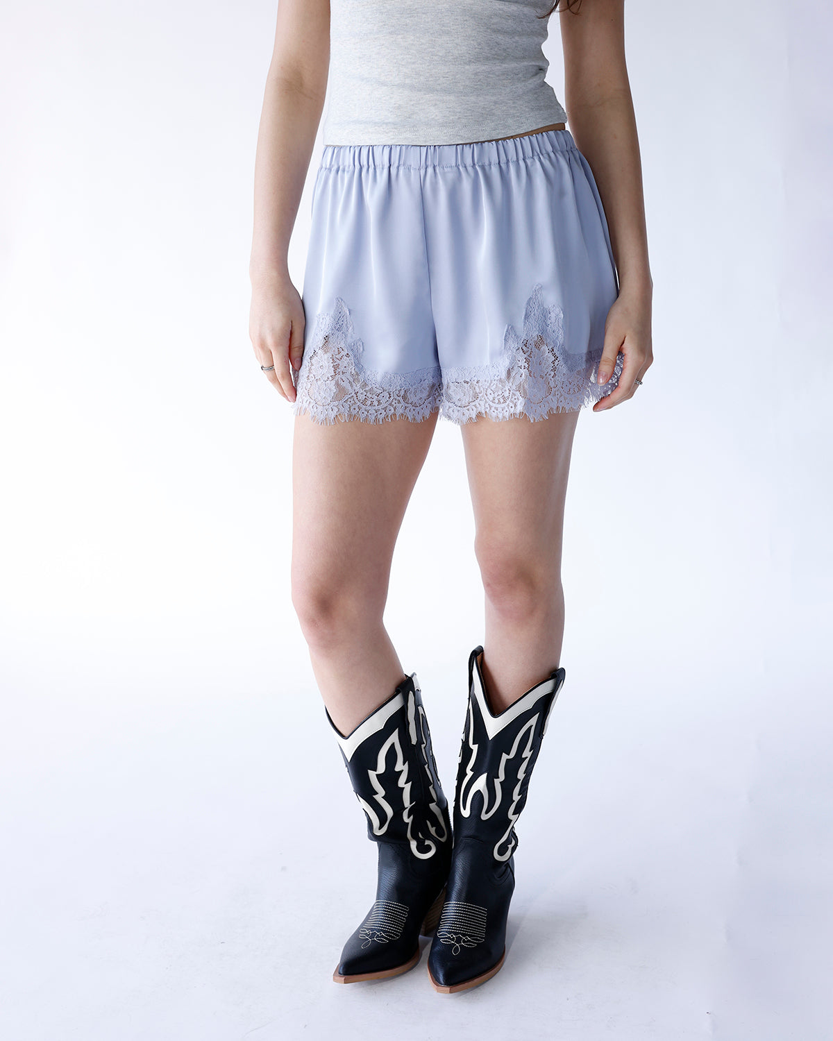 Baby blue satin shorts with white lace trim hem, paired with black cowboy boots