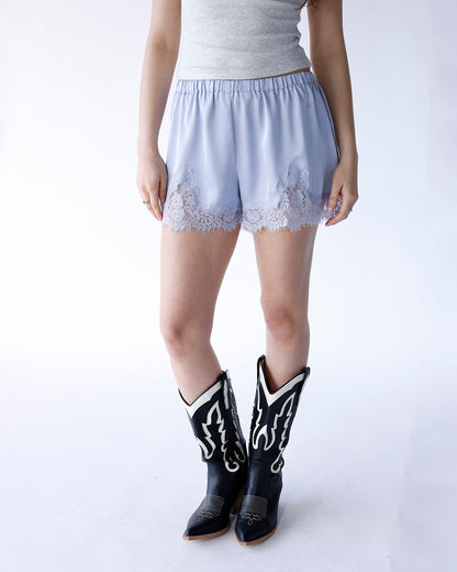 Baby blue satin shorts with white lace trim hem, paired with black cowboy boots