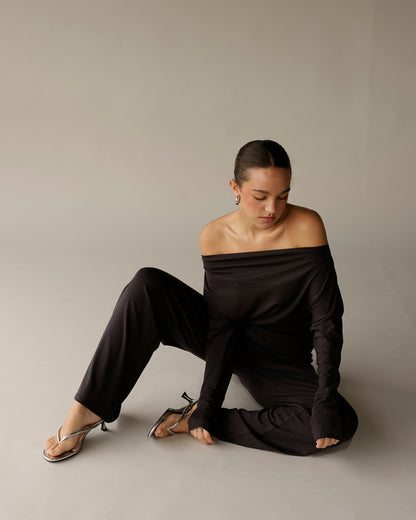 Black off-shoulder long-sleeve top with draped neckline, worn with black trousers