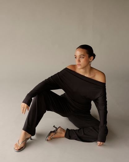 Black off-shoulder long sleeve draped top worn with black wide-leg pants