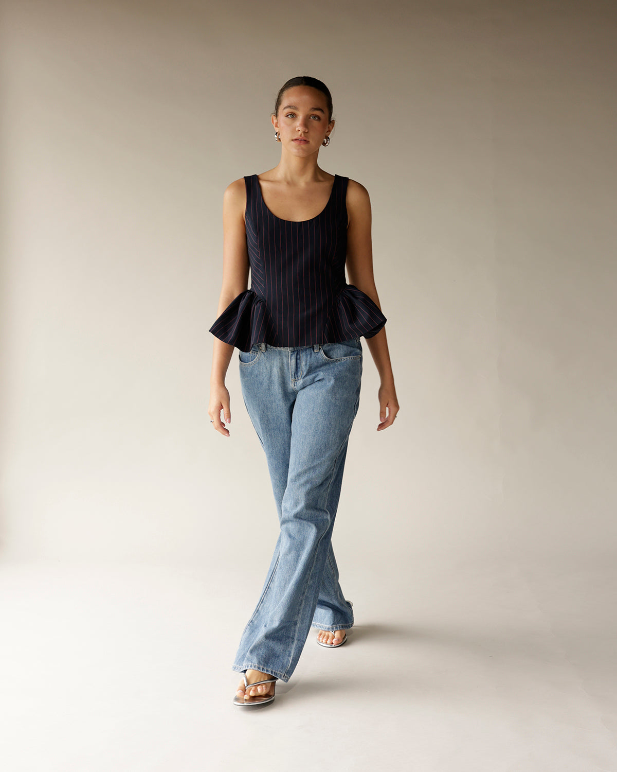 Navy pinstripe sleeveless peplum top with ruffled hem, paired with wide-leg jeans