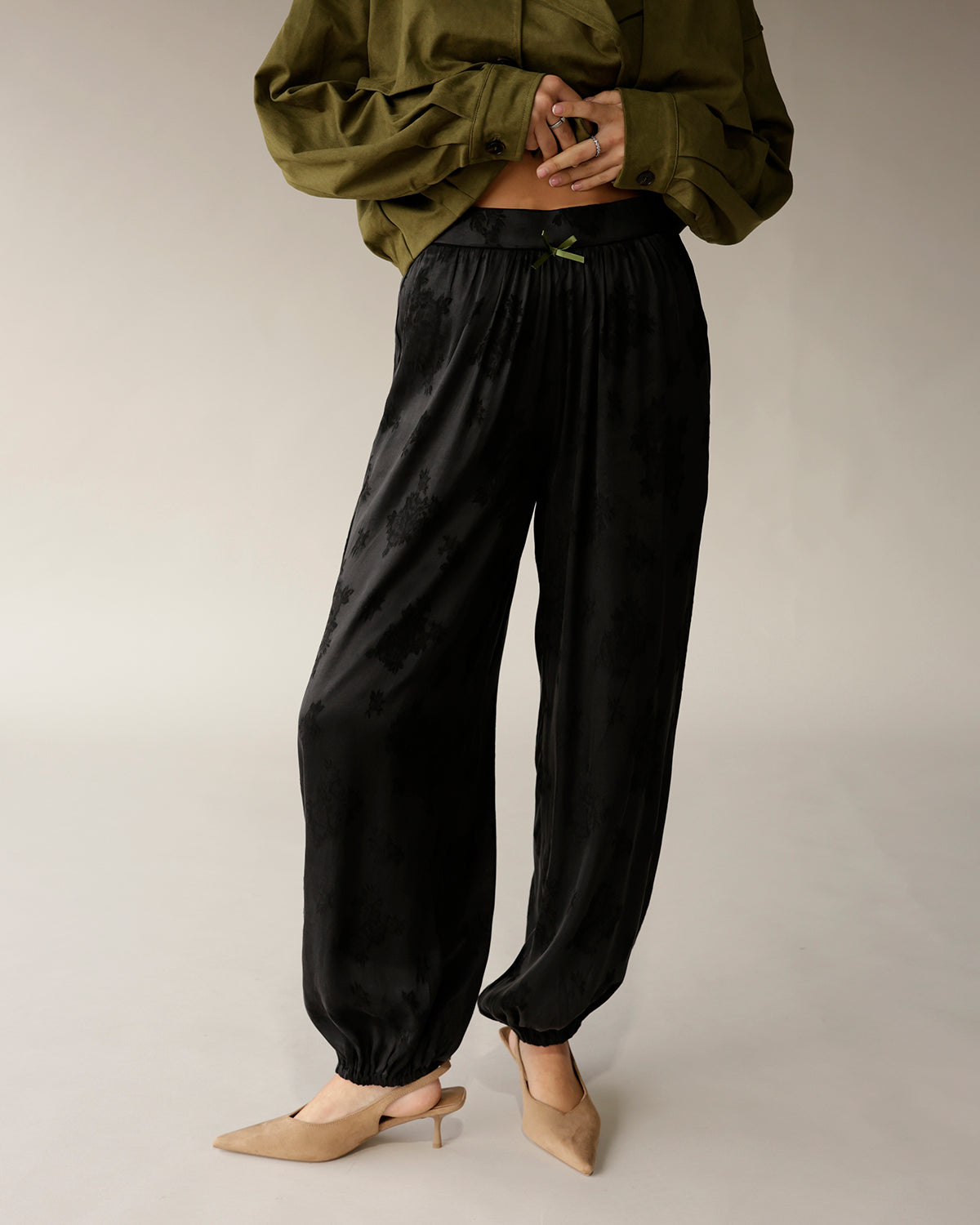 Black satin jacquard jogger pants with elastic cuffs and green ribbon waistband detail