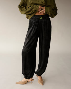 Black satin jacquard jogger pants with elastic cuffs and green ribbon waistband detail