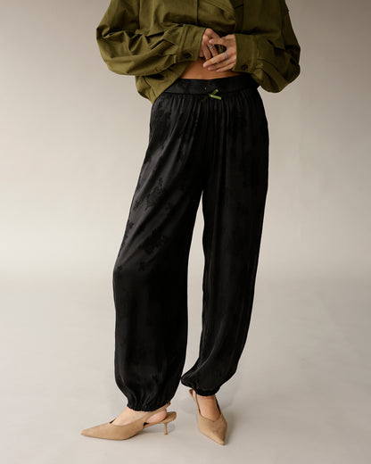 Black satin jacquard jogger pants with elastic cuffs and green ribbon waistband detail