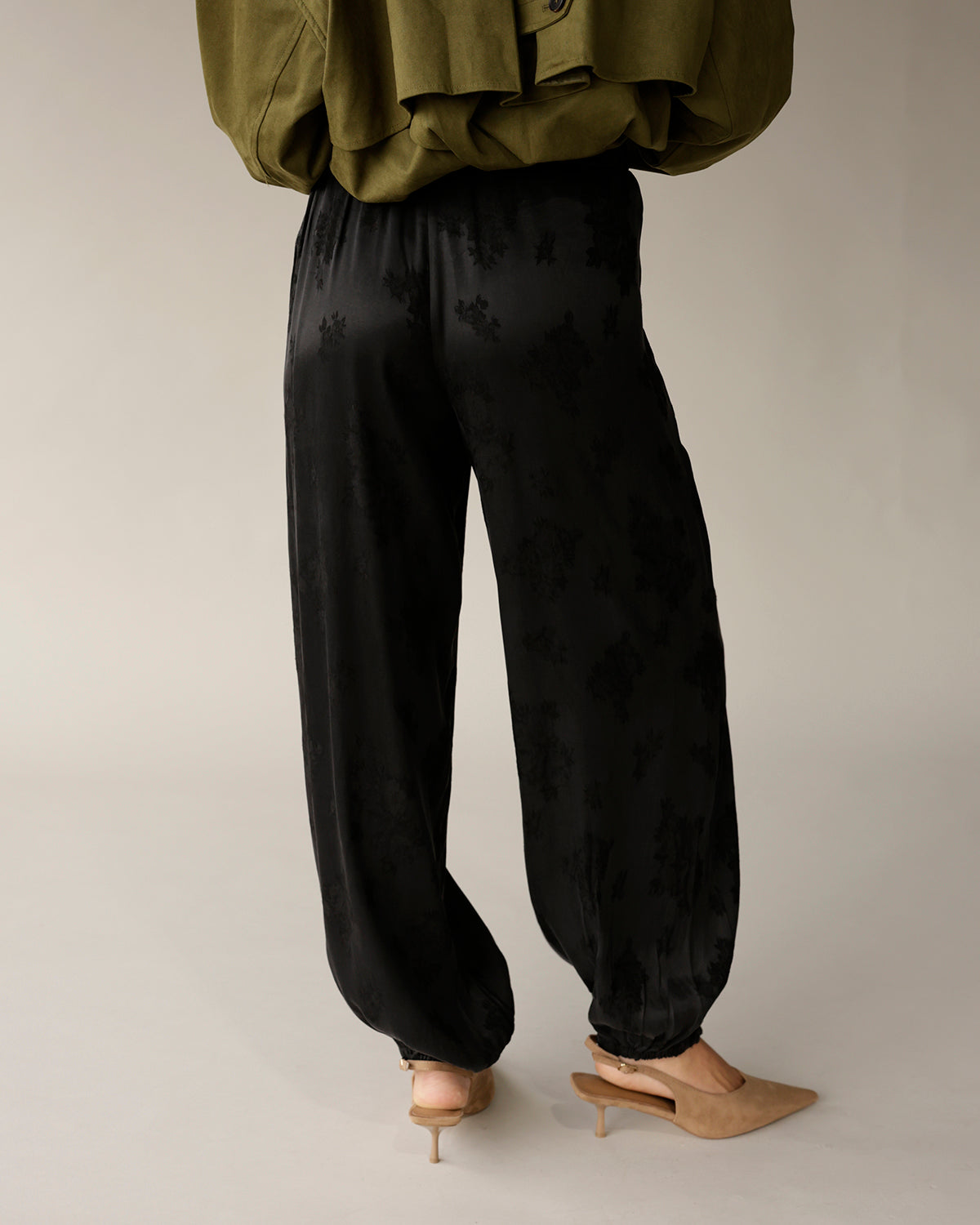 Black satin jacquard floral jogger pants with elastic cuffs, worn with nude heels