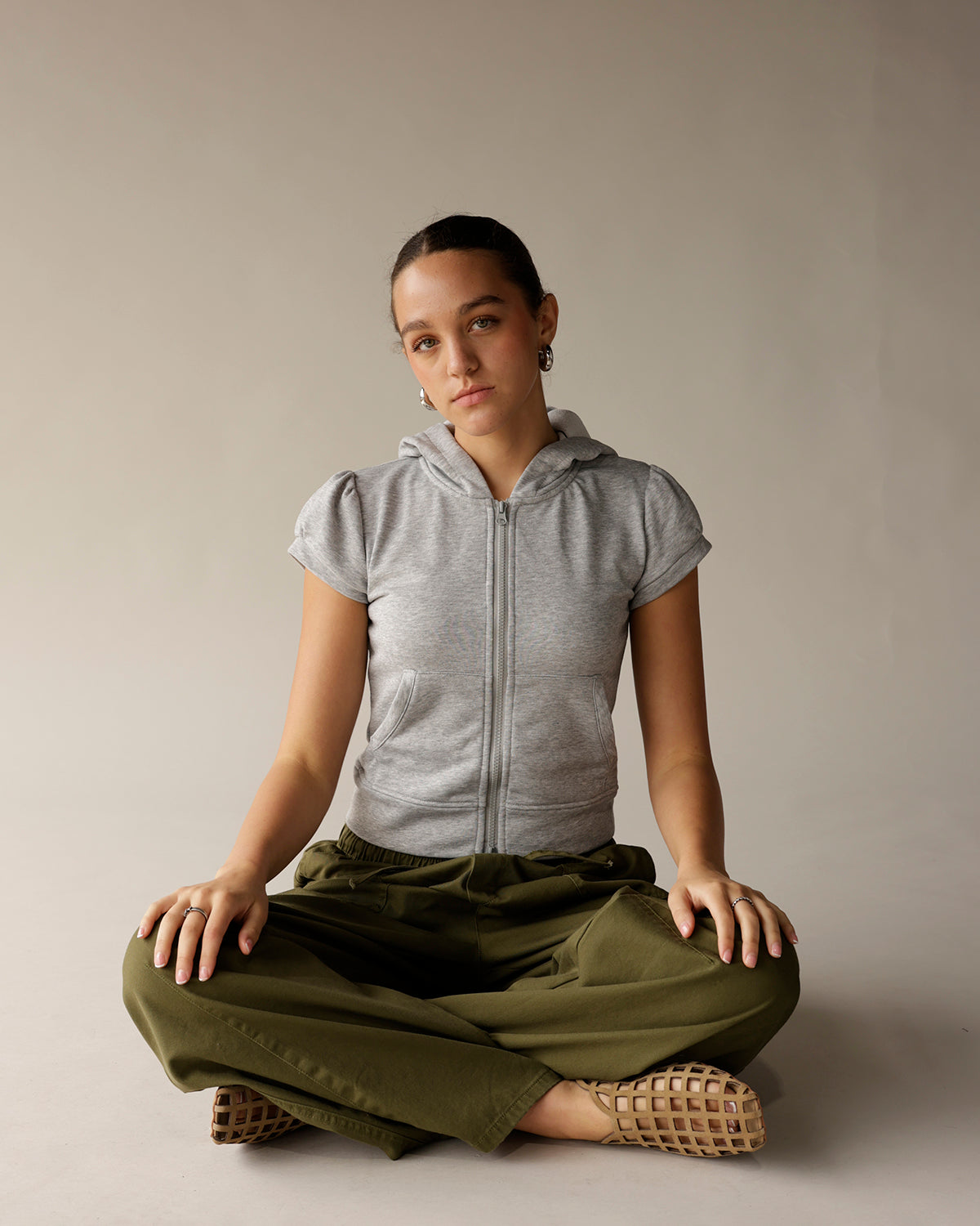 Olive green cargo barrel pants, wide leg, worn with gray zip hoodie, cross-legged pose.