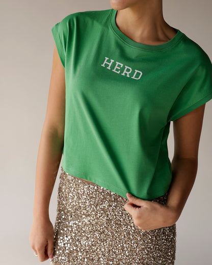 Kelly green cropped muscle tee with white HERD graphic, paired with gold sequin skirt