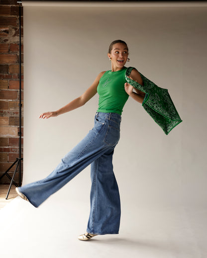 Kelly green paisley bandana tote bag carried over shoulder by jumping model