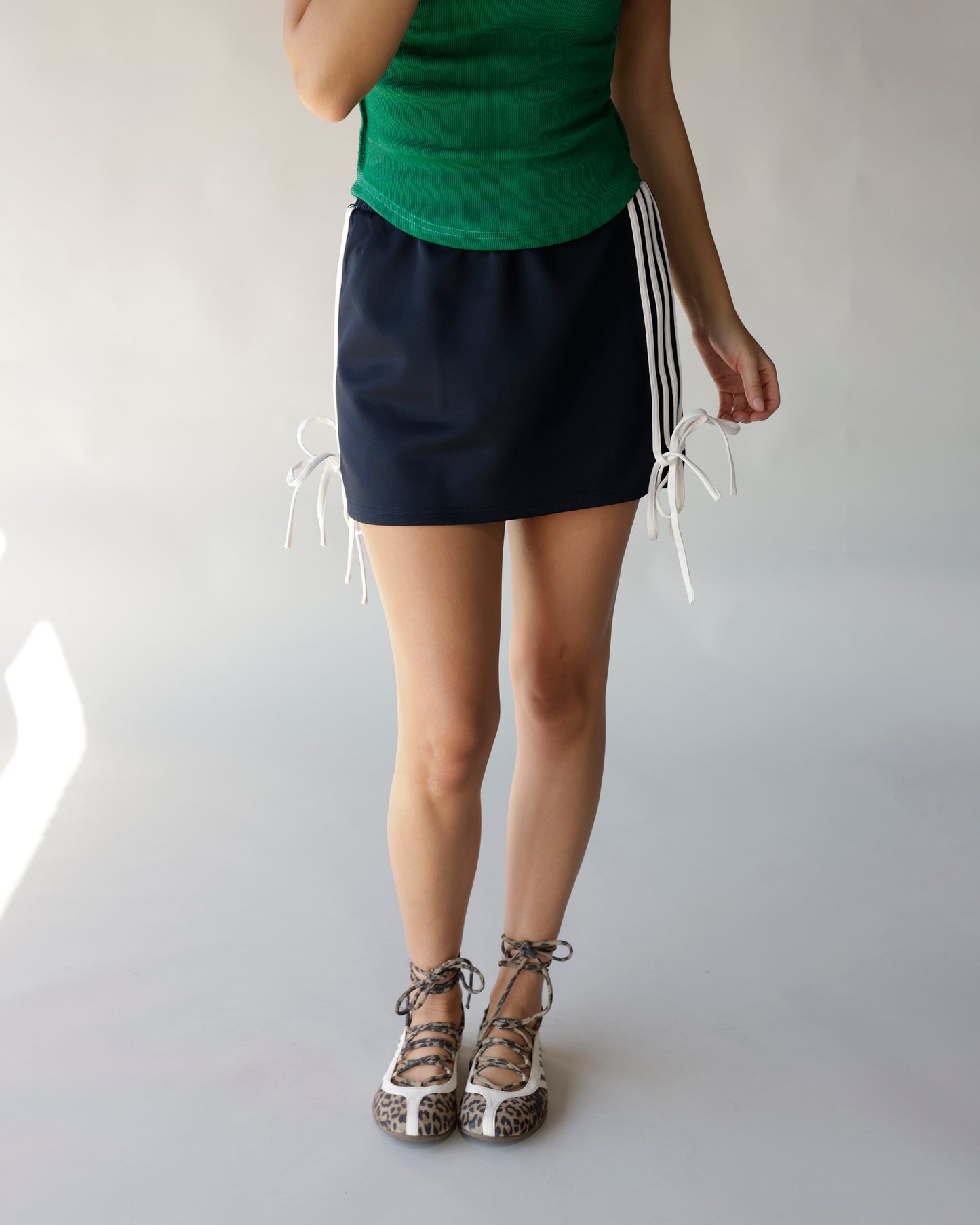 Black mini track skirt with white side stripe ties, paired with green top