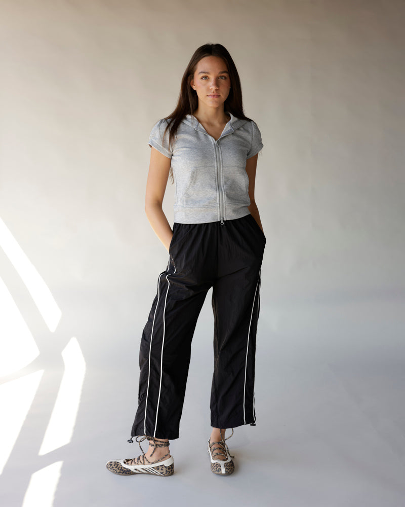 Black windbreaker pants with white side stripes, worn with gray zip hoodie