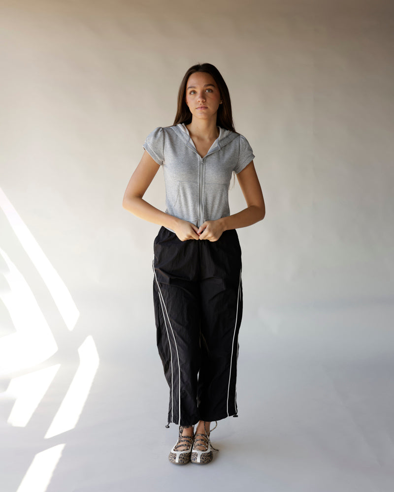 Black windbreaker pants with white side stripes, drawstring hem, worn with gray zip hoodie