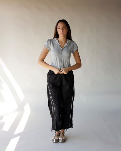 Black windbreaker pants with white side stripes, drawstring hem, worn with gray zip hoodie